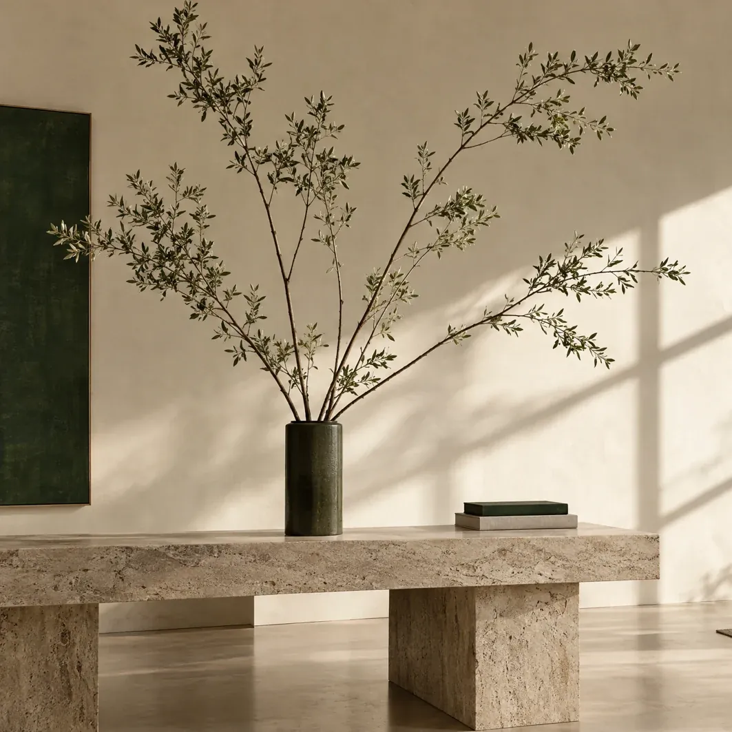 Tall olive branches arranged in a dark green vessel on a stone bench